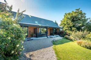 A modern house with a covered porch, a gravel driveway, and a well-maintained garden. - Alpine Garden Motel (Hanmer Springs)