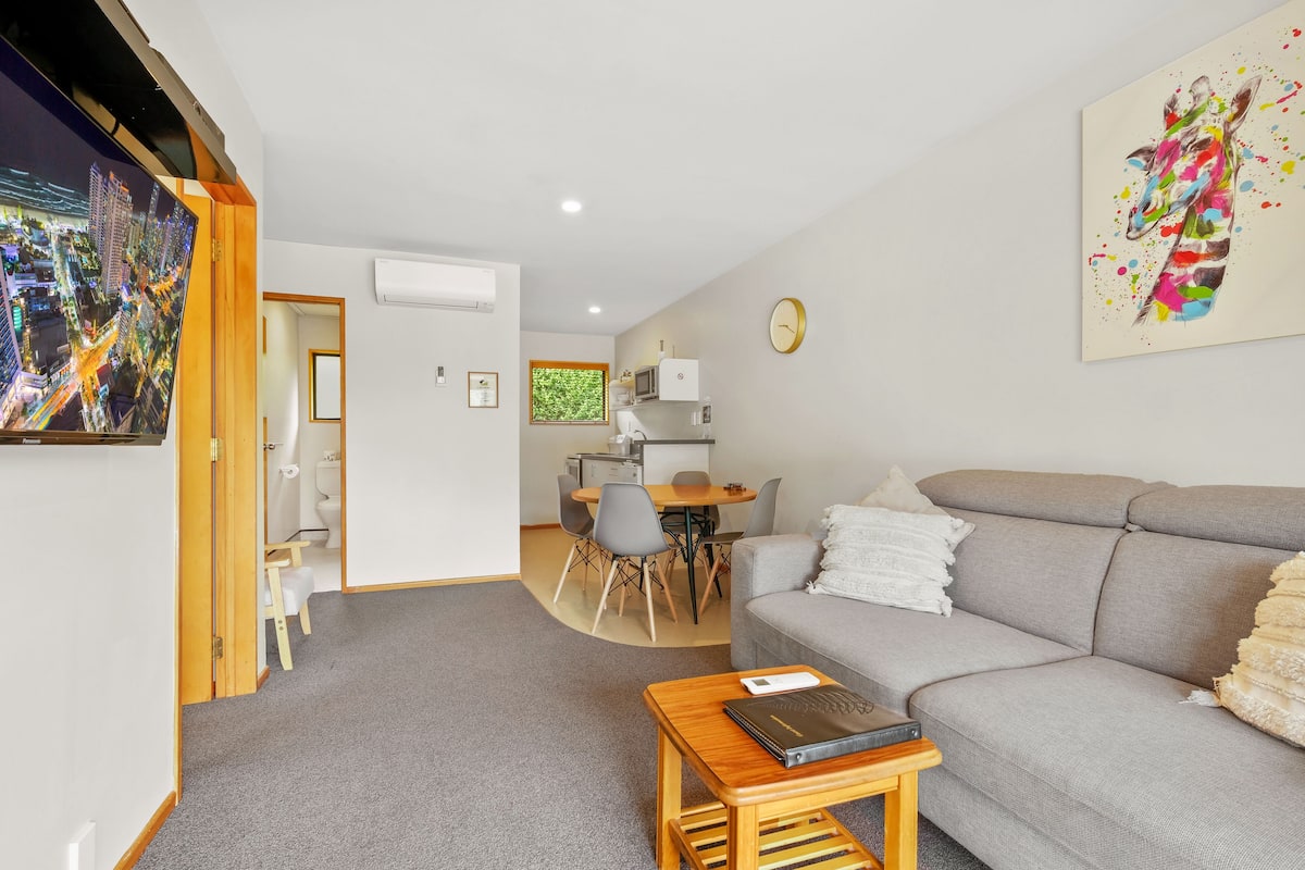 A modern living room with a grey sofa, a wooden coffee table, and a painting on the wall.