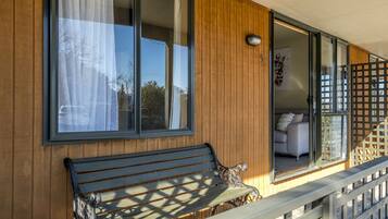 Pared exterior de madera con una banca, una puerta corrediza de vidrio y una pequeña zona de estar al aire libre.