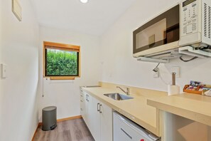 A compact kitchen with a built-in microwave, a sink, and a small trash bin. - Alpine Garden Motel (Hanmer Springs)