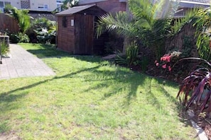 Un pequeño cobertizo de madera en un jardín, con un camino empedrado que lleva a él.