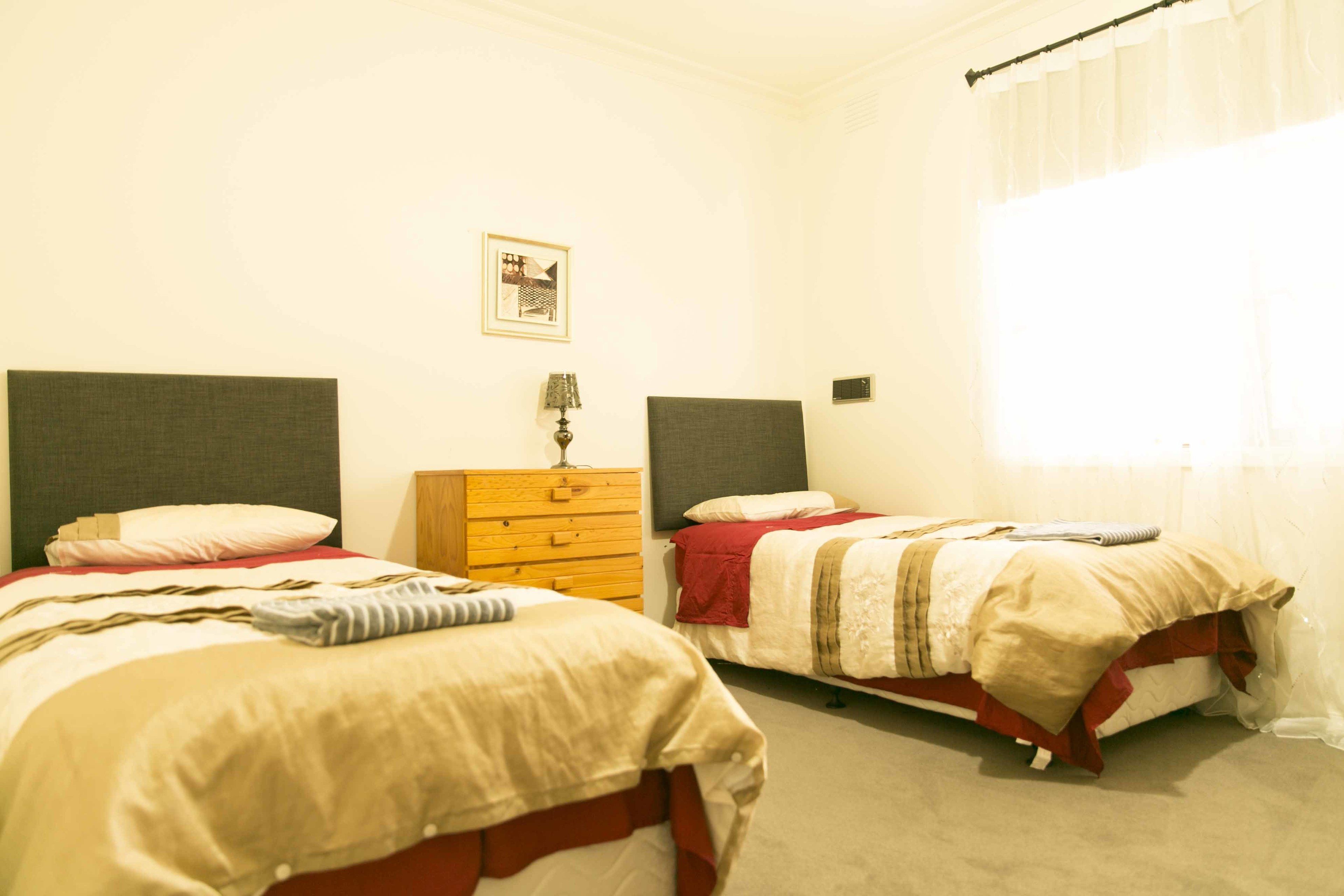 A bedroom with two beds, a wooden dresser, and a window with curtains.
