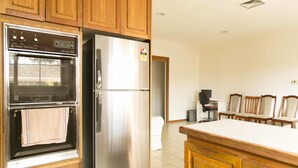 Una cocina con armarios de madera, un refrigerador de acero inoxidable, un horno y un comedor con sillas.