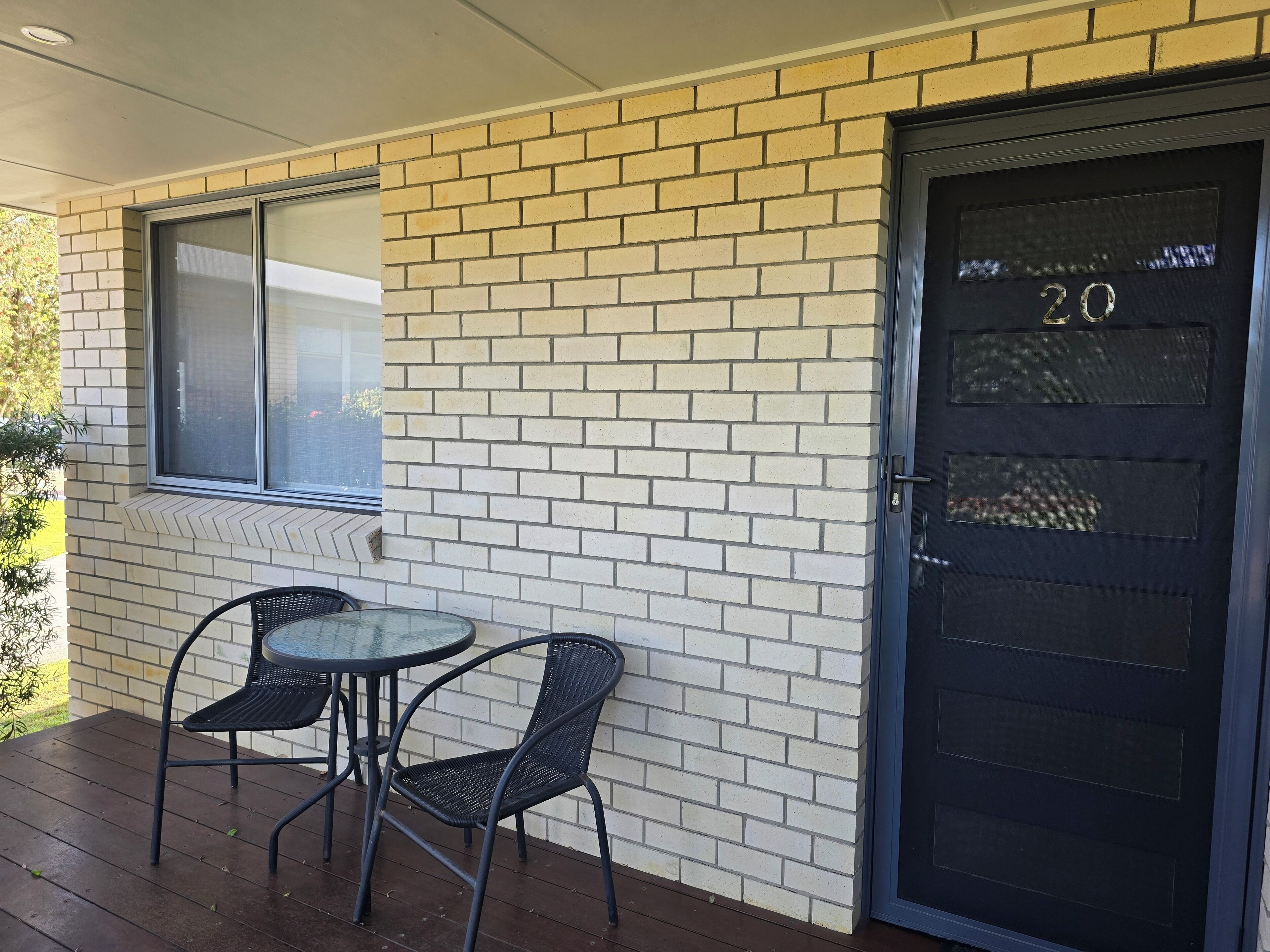 Un mur extérieur en briques avec une porte portant l’inscription « 20 » et une fenêtre située au-dessus d’une table et de chaises.