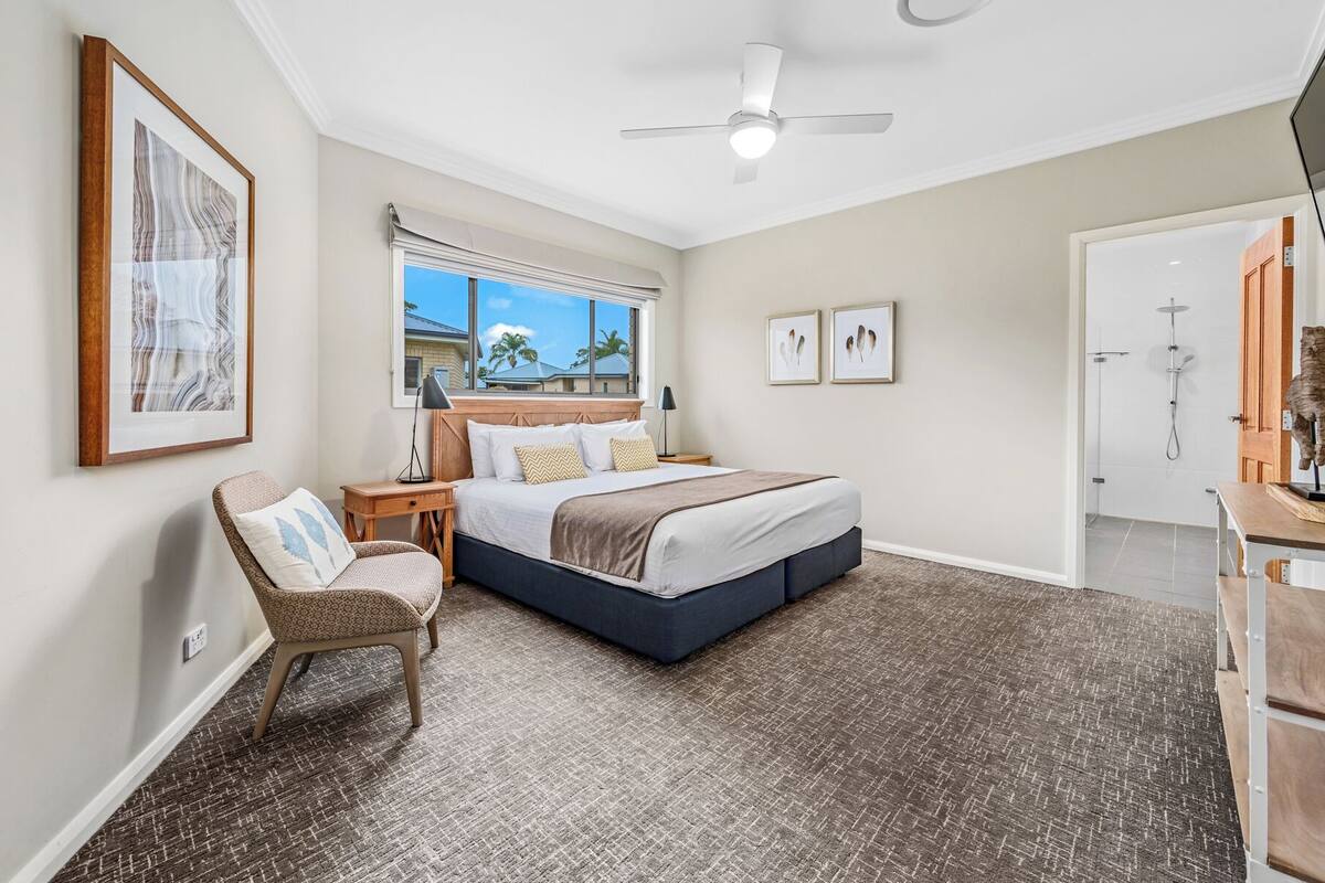 A bedroom with a bed, a chair, a desk, a ceiling fan, and a shower.