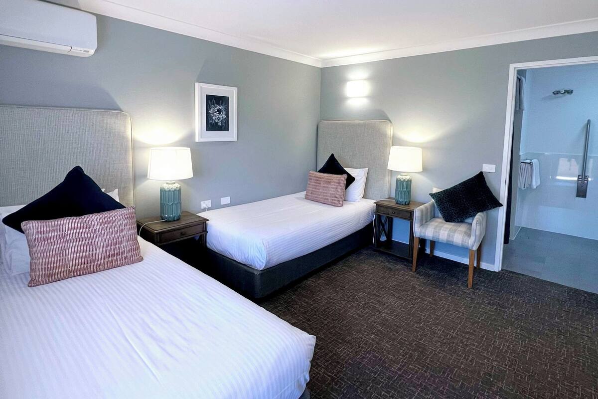 A hotel room with two beds, a chair, a desk, and a door.
