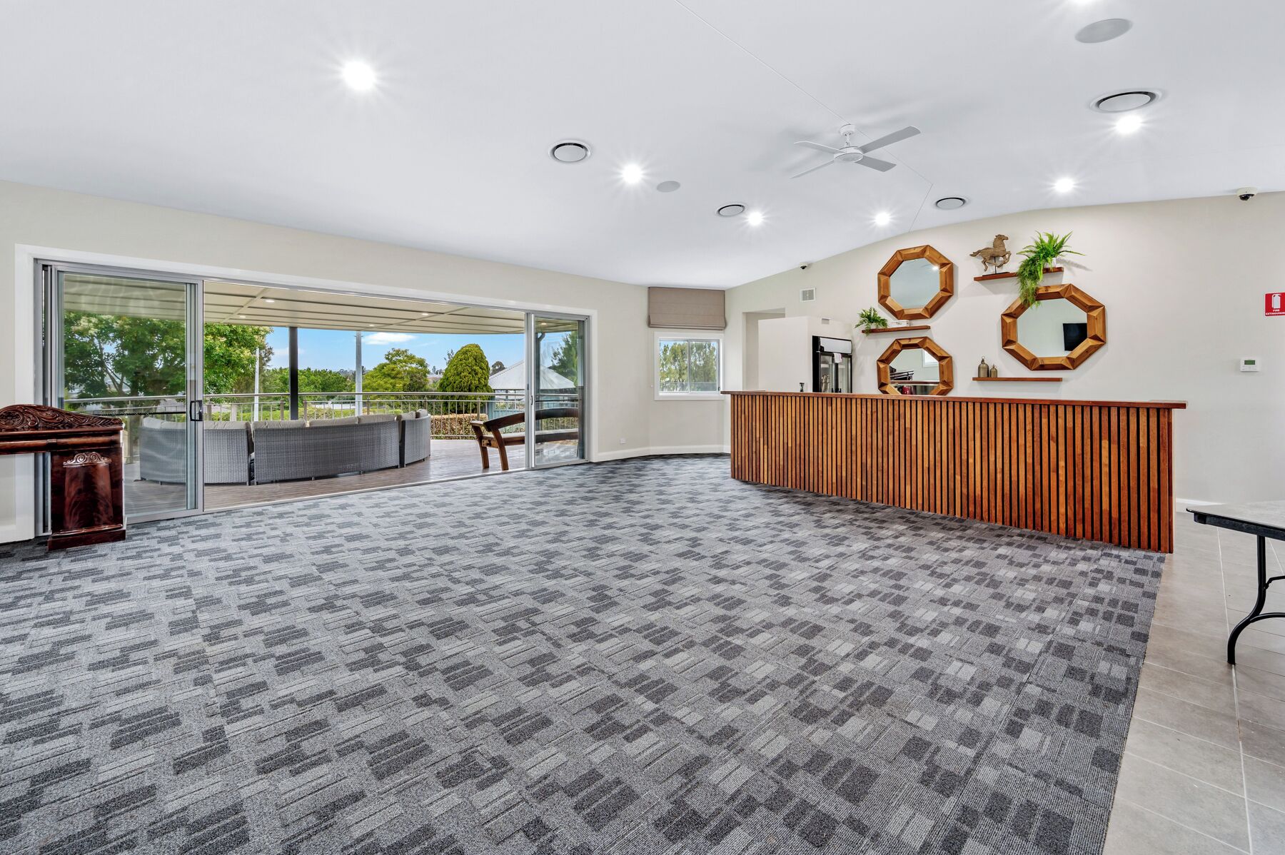 Un hall d’entrée spacieux, doté d’un tapis à carreaux, d’un comptoir de réception en bois et d’une porte vitrée donnant sur un espace extérieur aménagé pour s’asseoir.