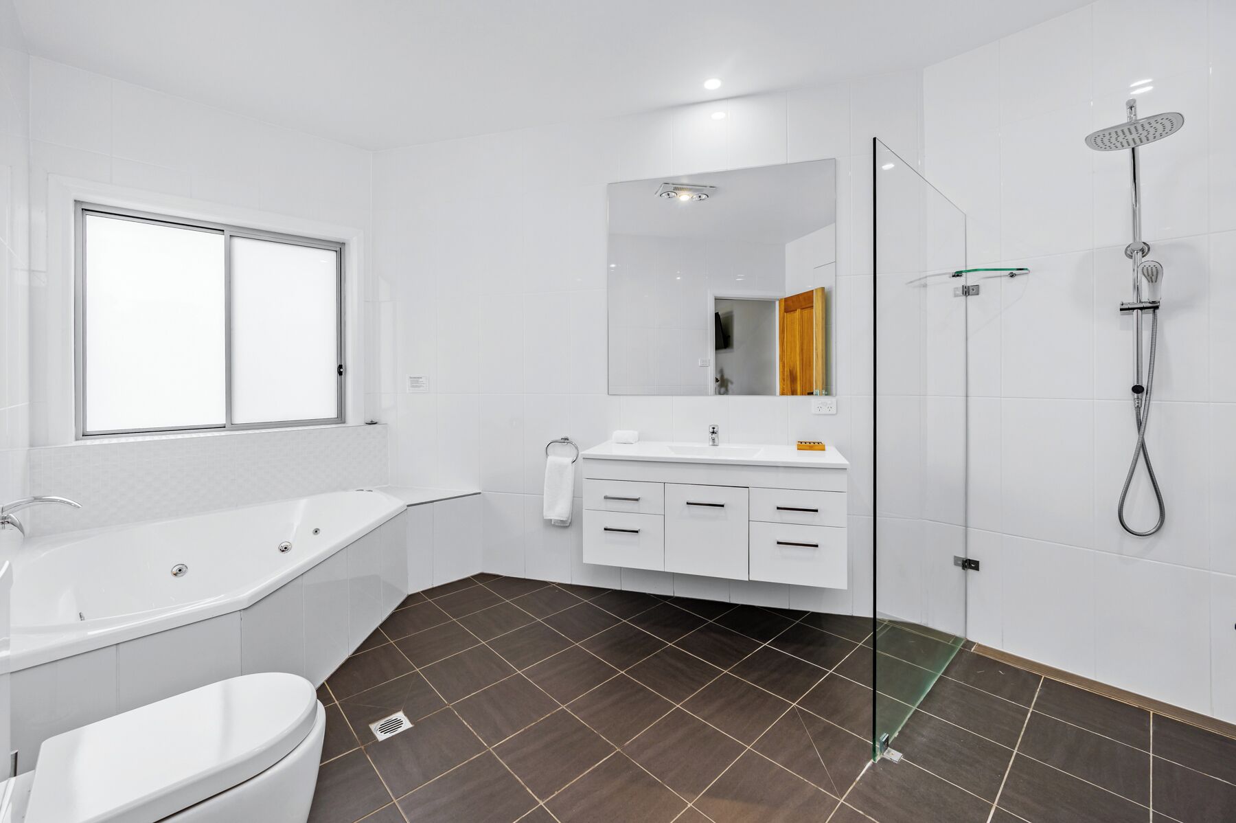 A modern bathroom with a bathtub, toilet, vanity with drawers, a mirror, and a glass-enclosed shower.