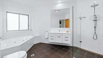 A modern bathroom with a bathtub, toilet, vanity with drawers, a mirror, and a glass-enclosed shower.