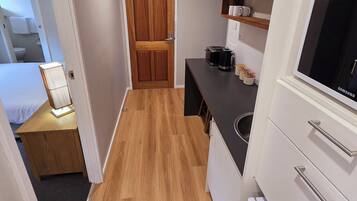 Cocina compacta con piso de madera, horno microondas integrado, televisor Samsung y un pequeño espacio de descanso con mesa y silla.