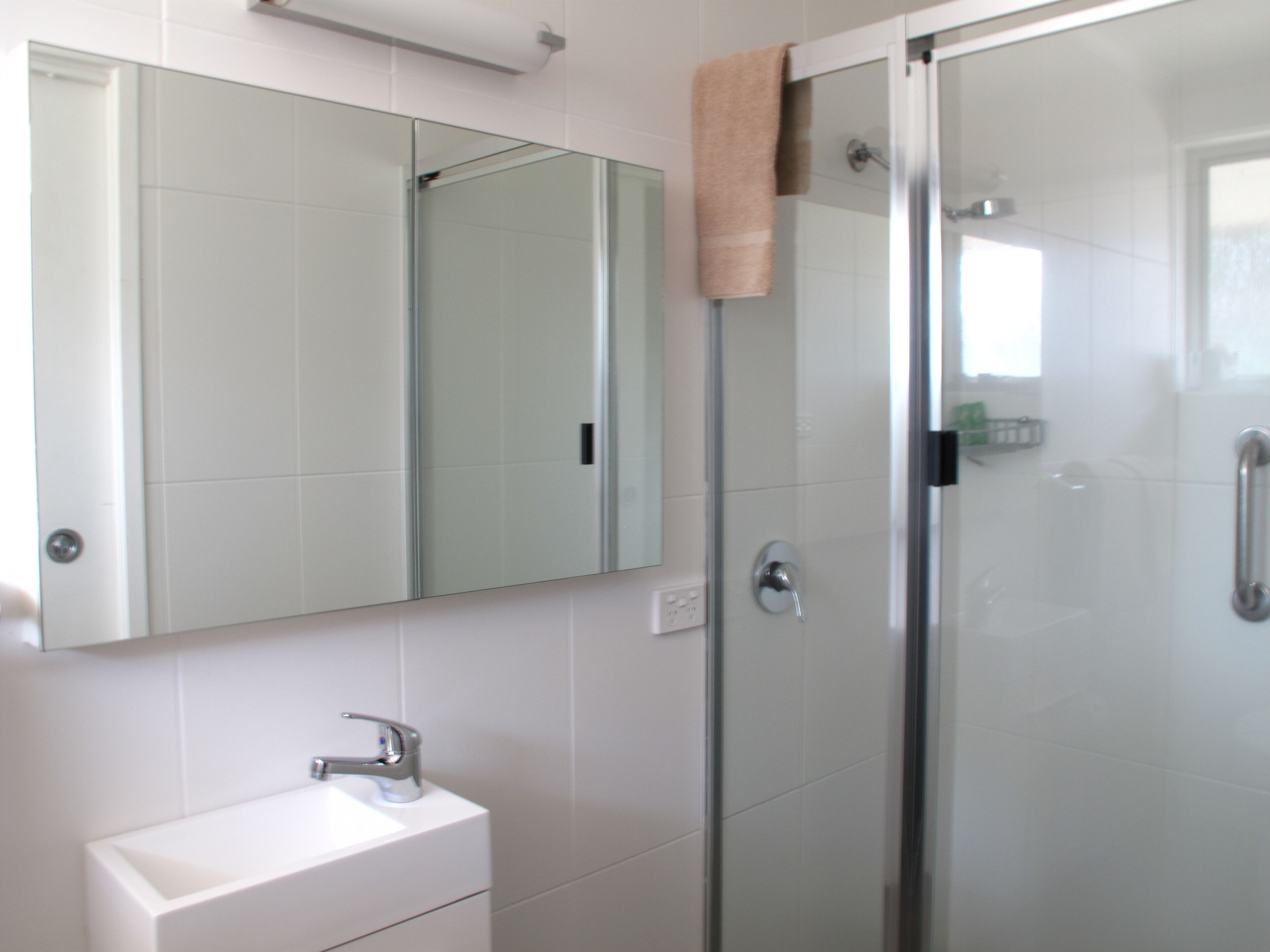 A bathroom with a glass shower enclosure, a white sink, and a mirror above the sink.