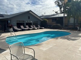 Una piscina con sillas de descanso, una silla metálica y un edificio de techo plano y ventanas.