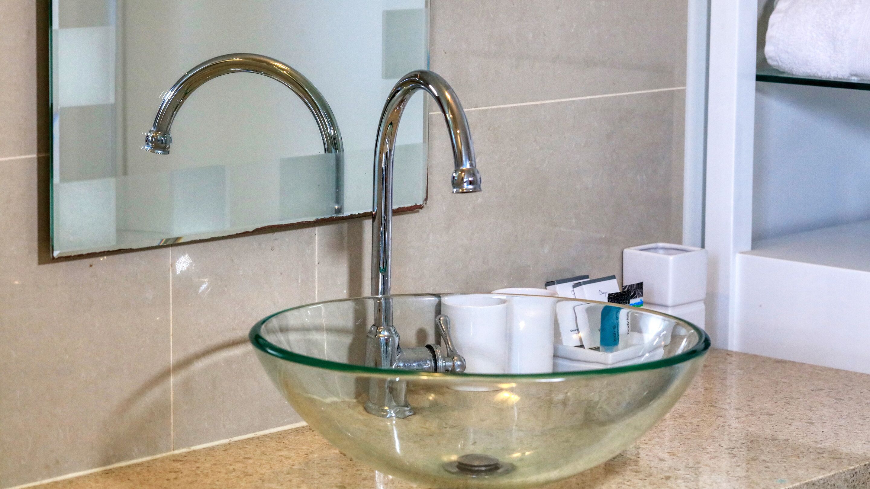 A modern bathroom with a glass bowl sink, a chrome faucet, and a mirror above it.