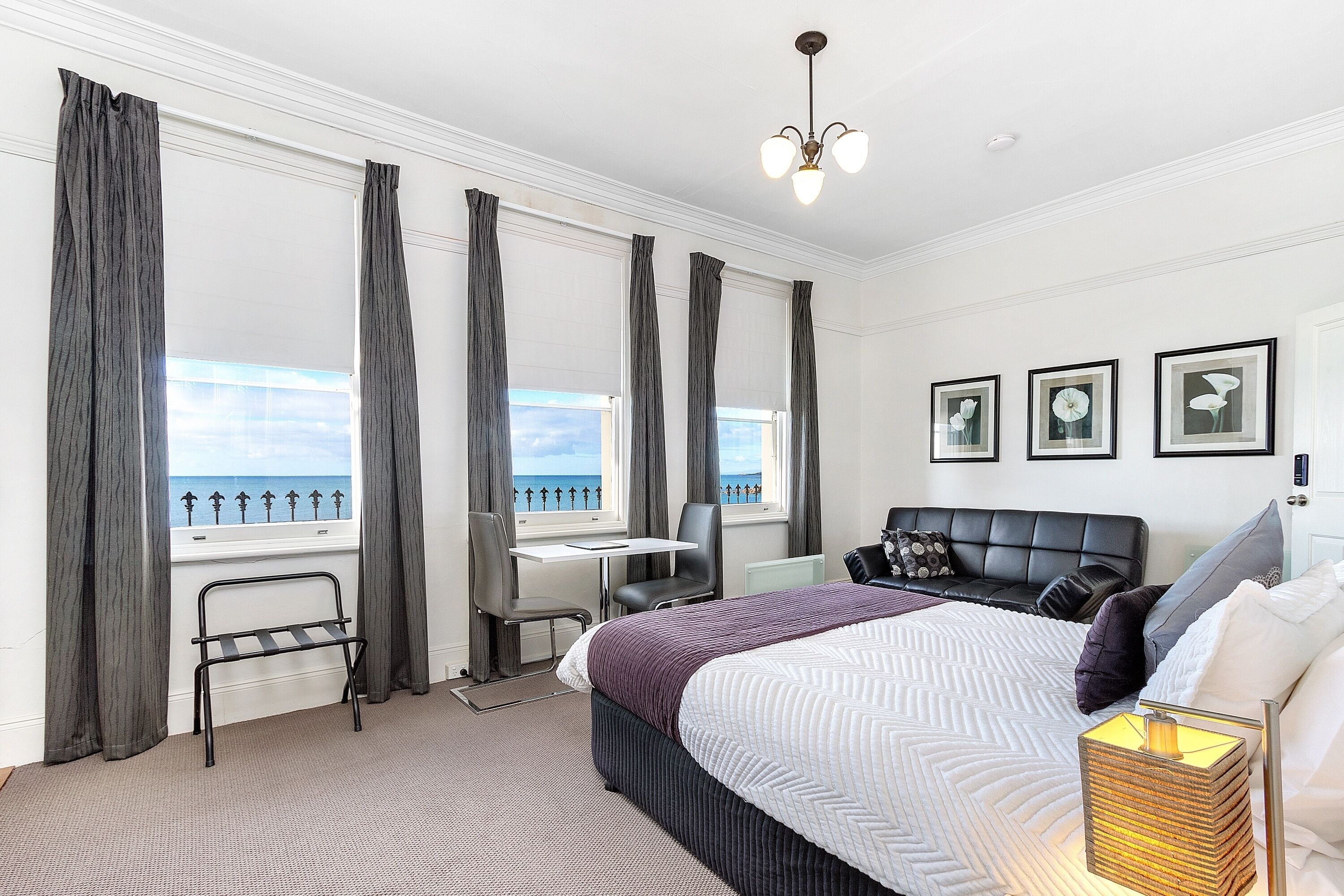 A hotel room with a bed, a desk, a chair, and a view of the sea.