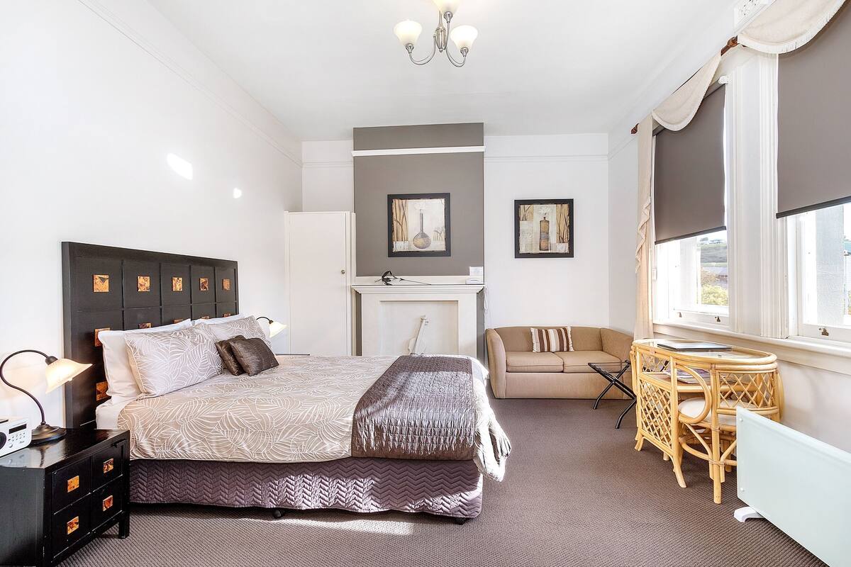 A bedroom with a bed, bedside table, lamp, and a window with curtains.