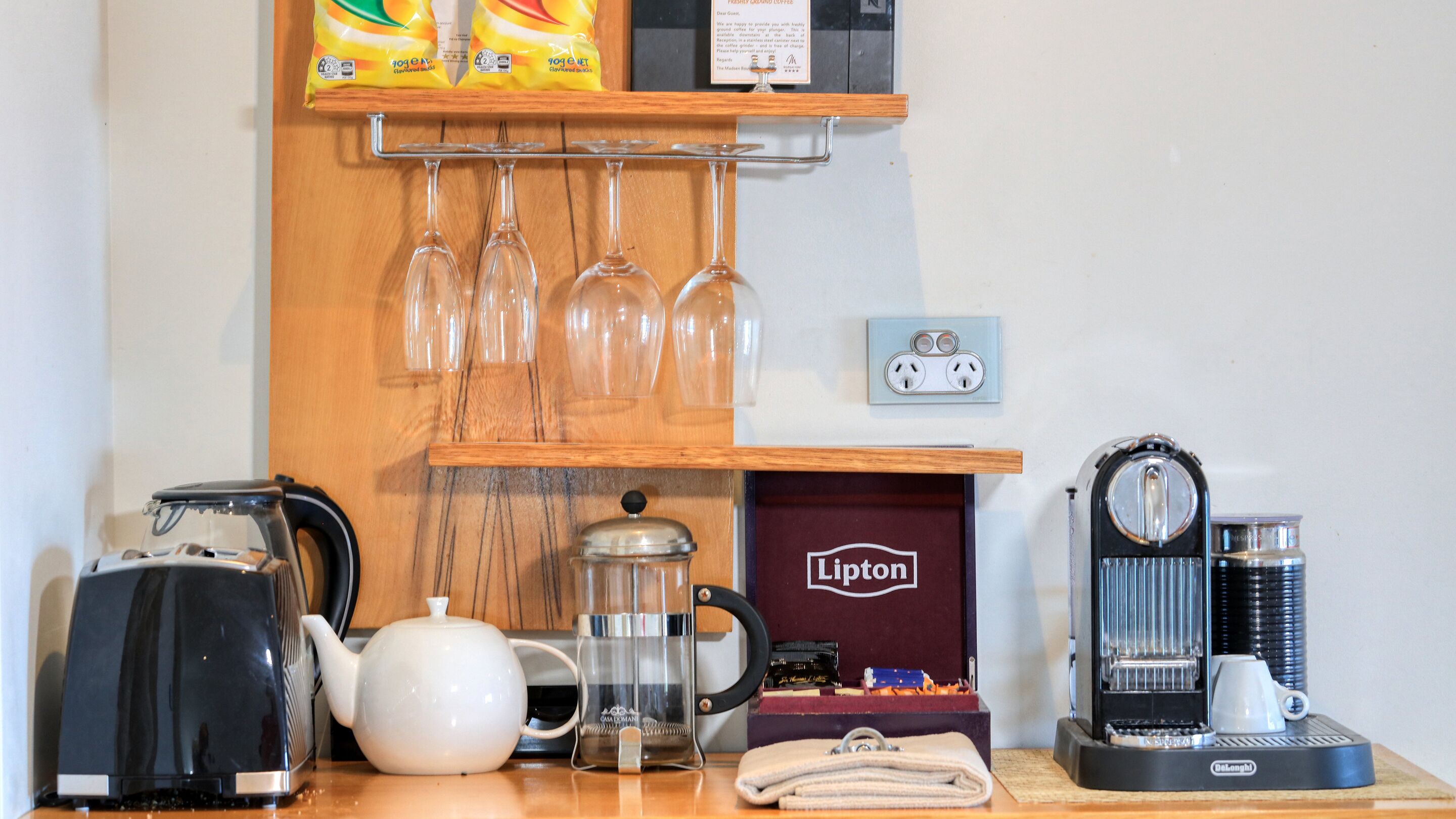Angolo caffè con bollitore, macchina da caffè, scatola di tè Lipton e ripiano con confezioni di caffè e bicchieri.