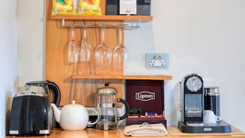 Angolo caffè con bollitore, macchina da caffè, scatola di tè Lipton e ripiano con confezioni di caffè e bicchieri.