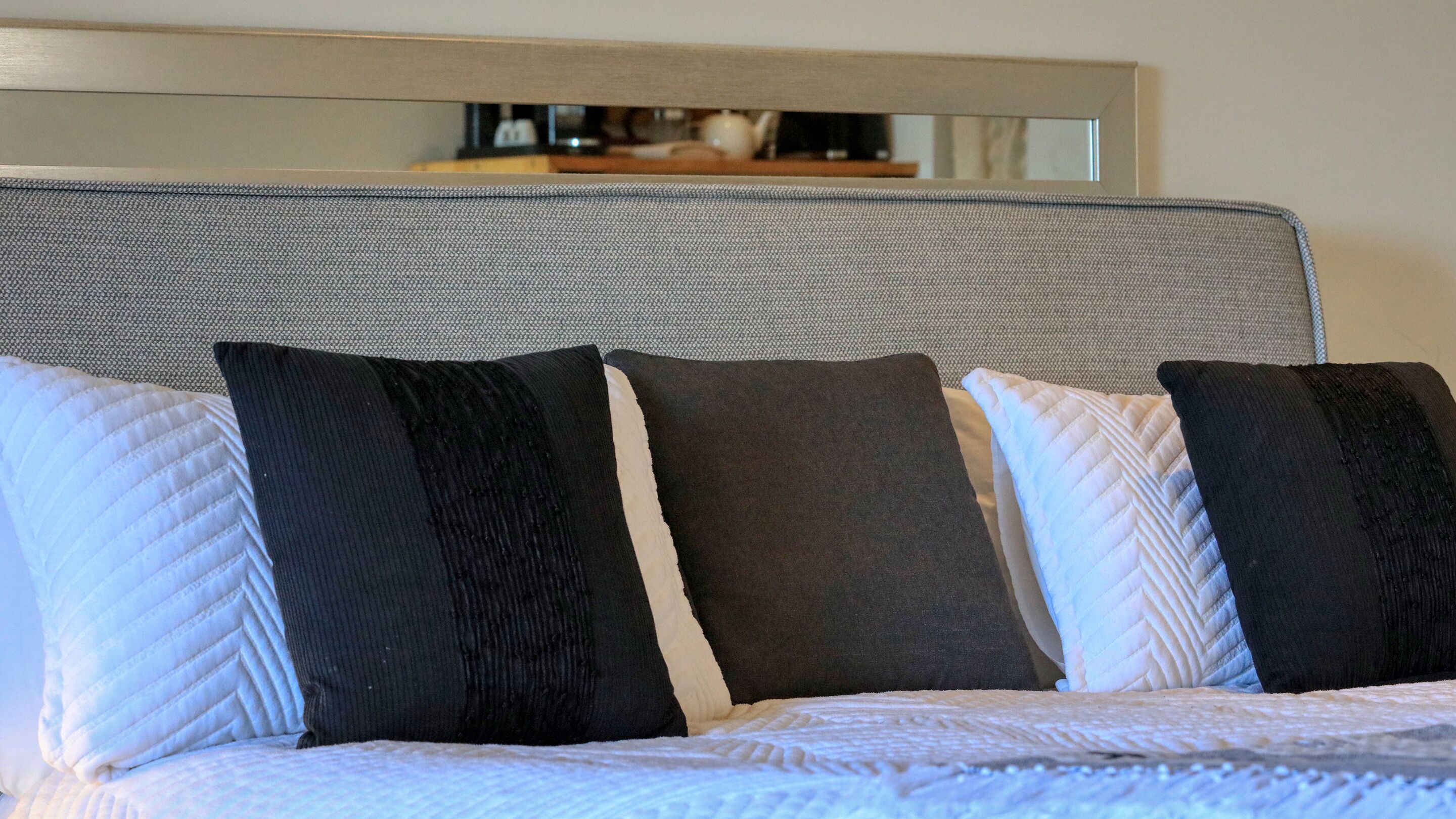 Una cama con cabecera gris y cuatro almohadas en tonos negros, blancos y grises.