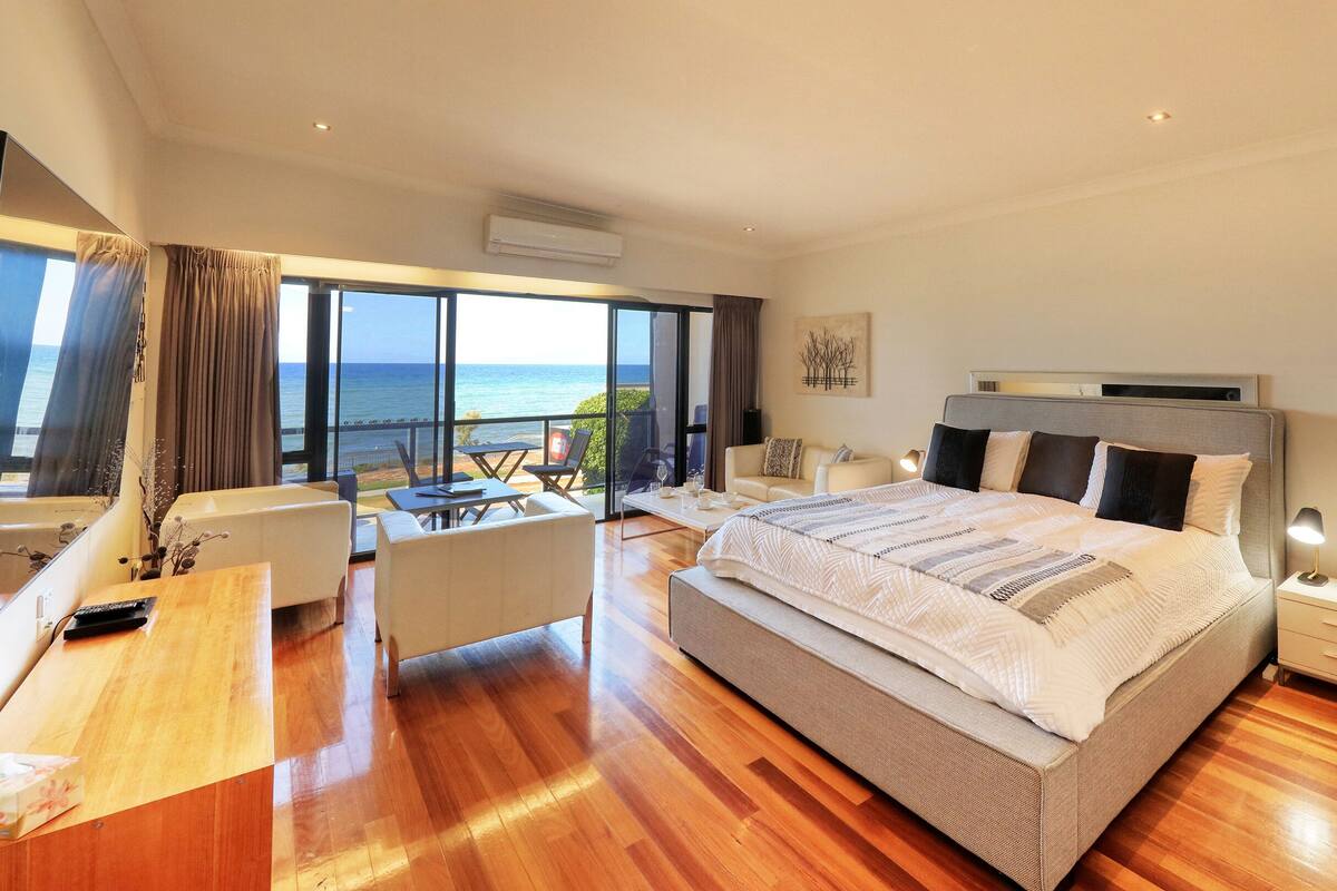 A spacious bedroom with a large bed, a desk, and a balcony with a view of the sea.