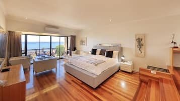 A spacious bedroom with a large bed, a sitting area with a view of the sea, and a balcony.