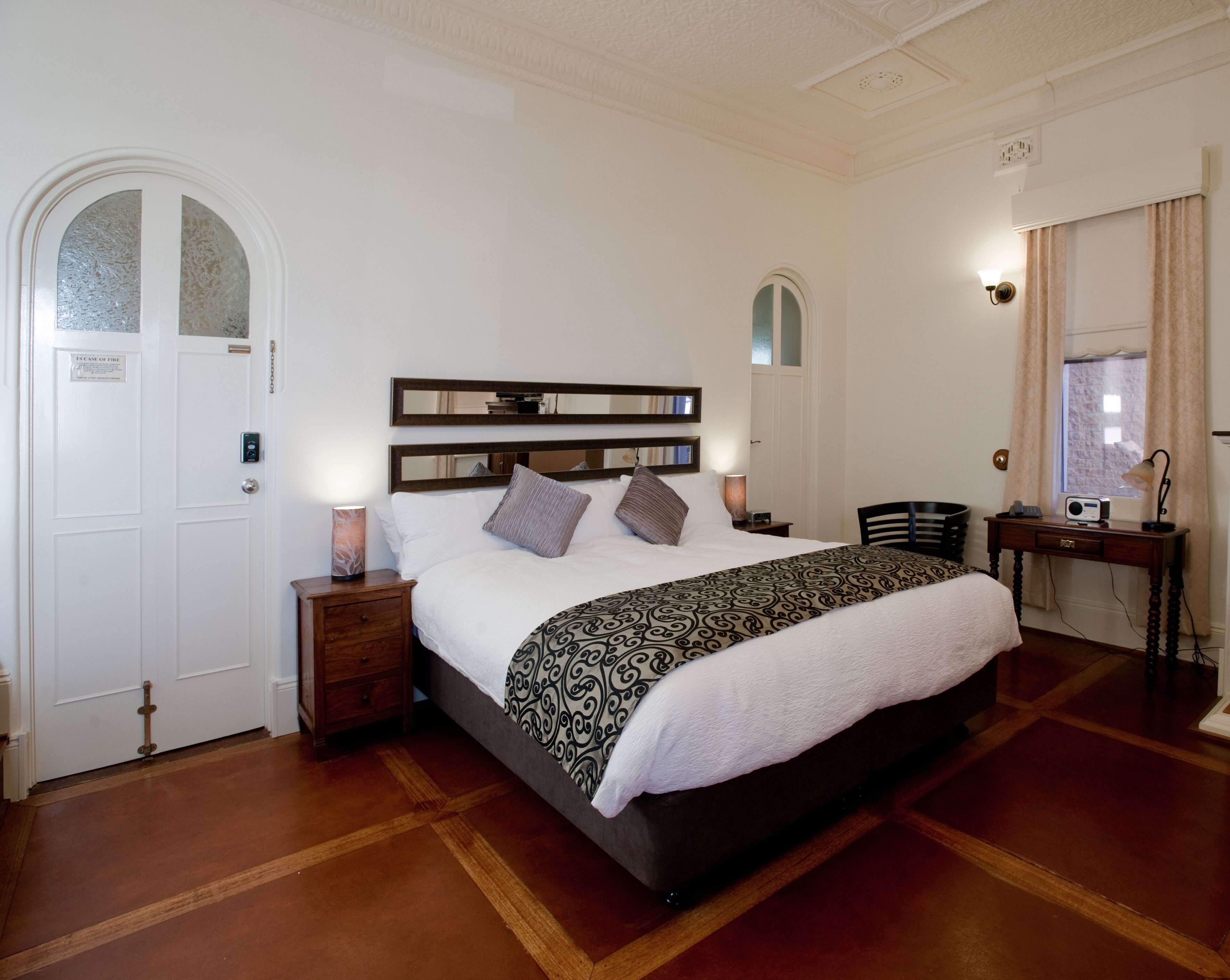 A neatly arranged bedroom with a large bed, bedside tables, a desk, and a chair.