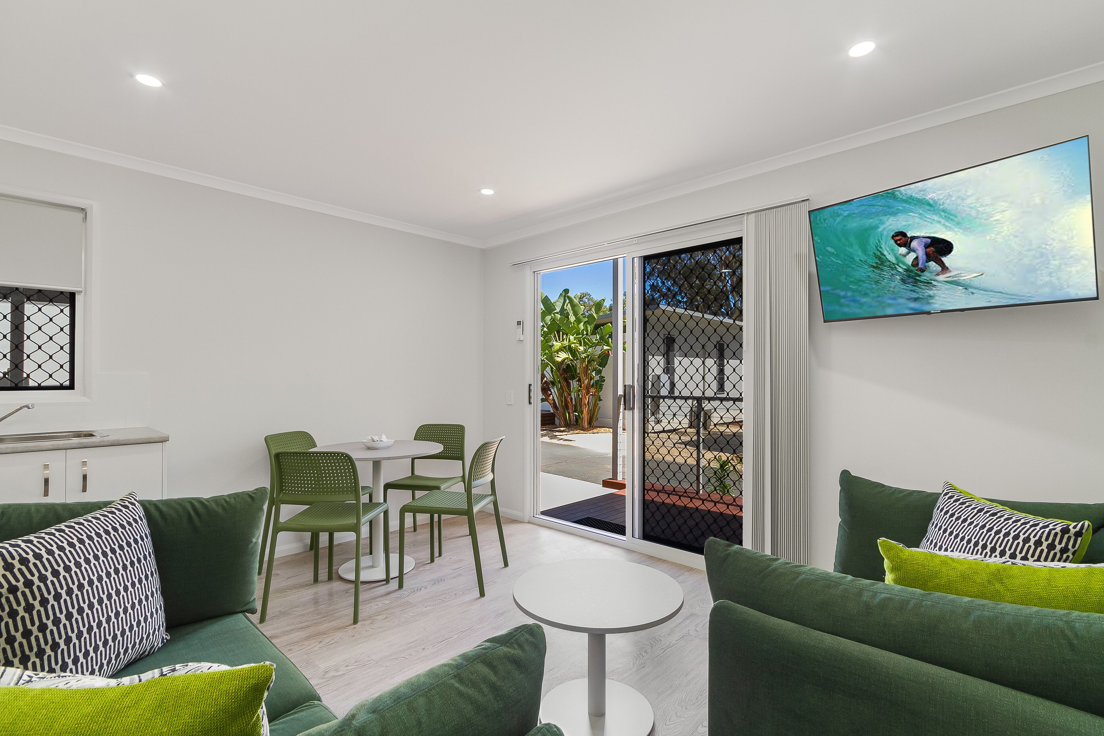 A modern living room with green sofas, a white coffee table, and a TV displaying a surfer.