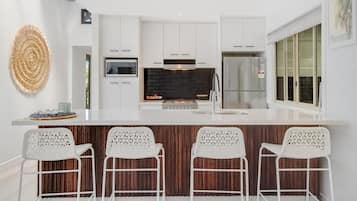 A modern kitchen with white cabinetry, a central island with bar stools, a black backsplash, and a stainless steel refrigerator.