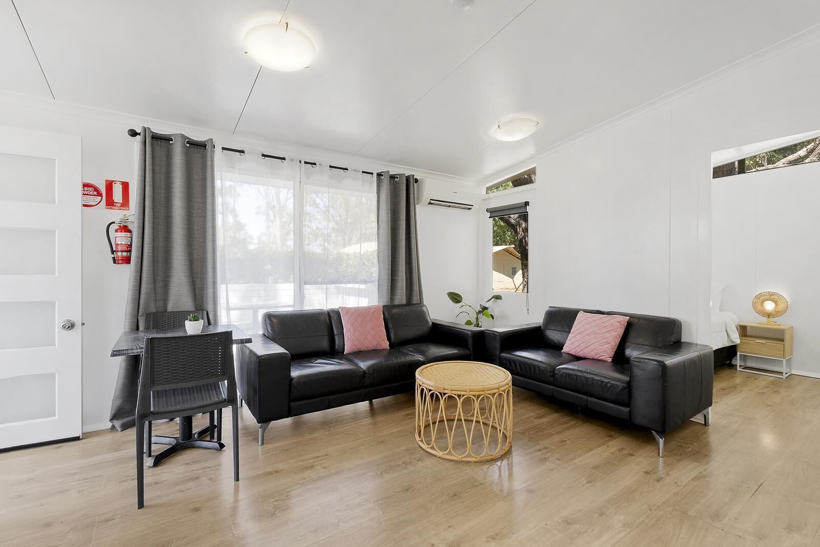 A modern living room with a black leather sofa, a round wicker coffee table, and a small side table with a lamp.