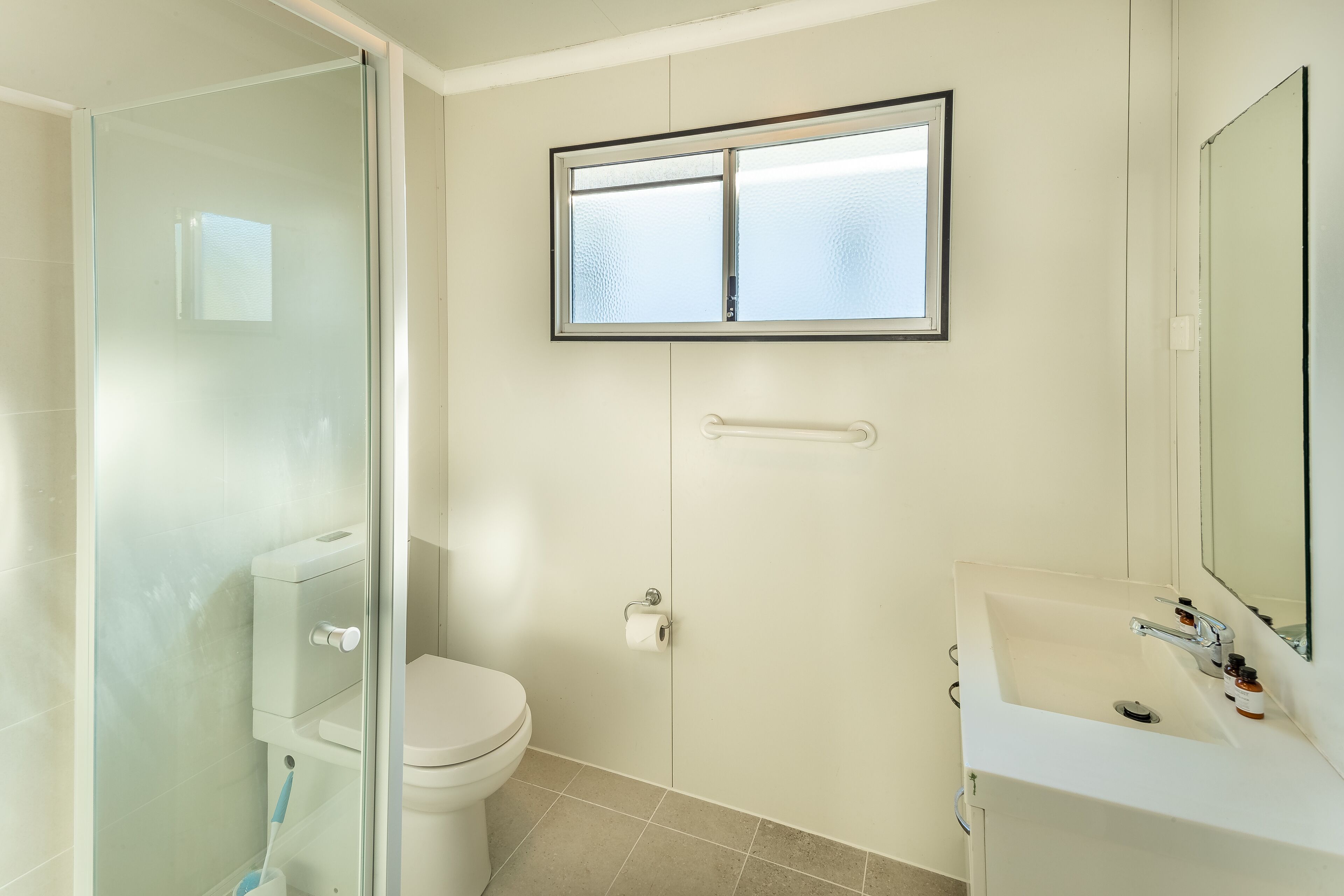A bathroom with a toilet, a sink, a glass shower enclosure, and a window.