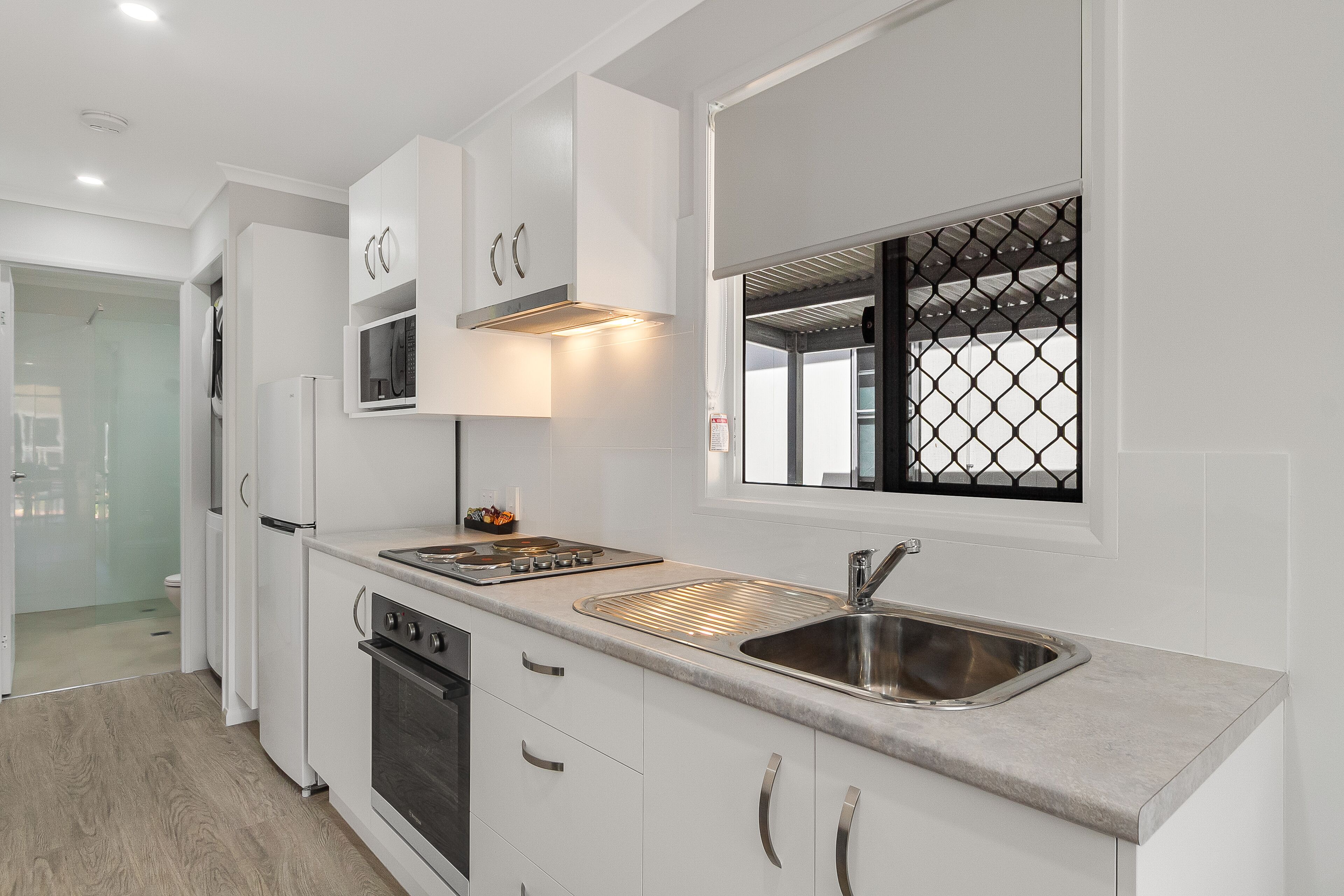 A modern kitchen with white cabinets, stainless steel appliances, and a large window with a metal grid.