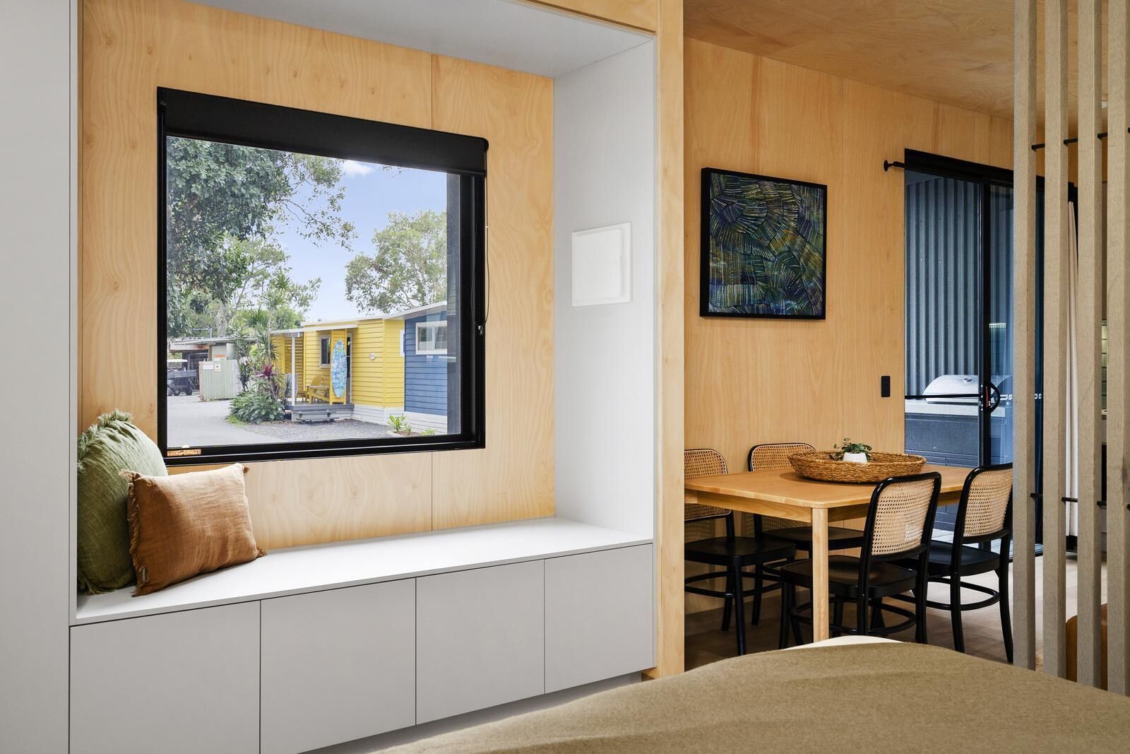 Una habitación con un banco empotrado debajo de un ventanal grande, una mesa de comedor con sillas y un cuadro en la pared.