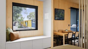 Una habitación con un banco empotrado debajo de un ventanal grande, una mesa de comedor con sillas y un cuadro en la pared.
