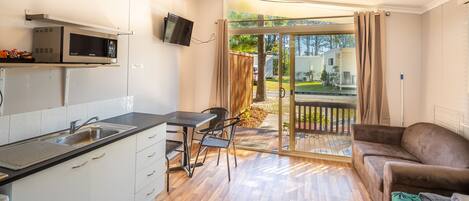 A compact kitchen with a microwave, sink, and dining area. A sliding glass door leads to an outdoor deck with a view of a residential area.