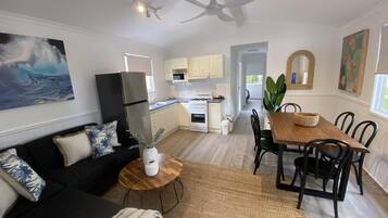 A modern kitchen with white cabinets, a refrigerator, and a microwave. There is a dining area with a wooden table and chairs.