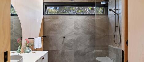 A modern bathroom with a glass shower enclosure, a large mirror, and a vanity with a sink and decorative items.