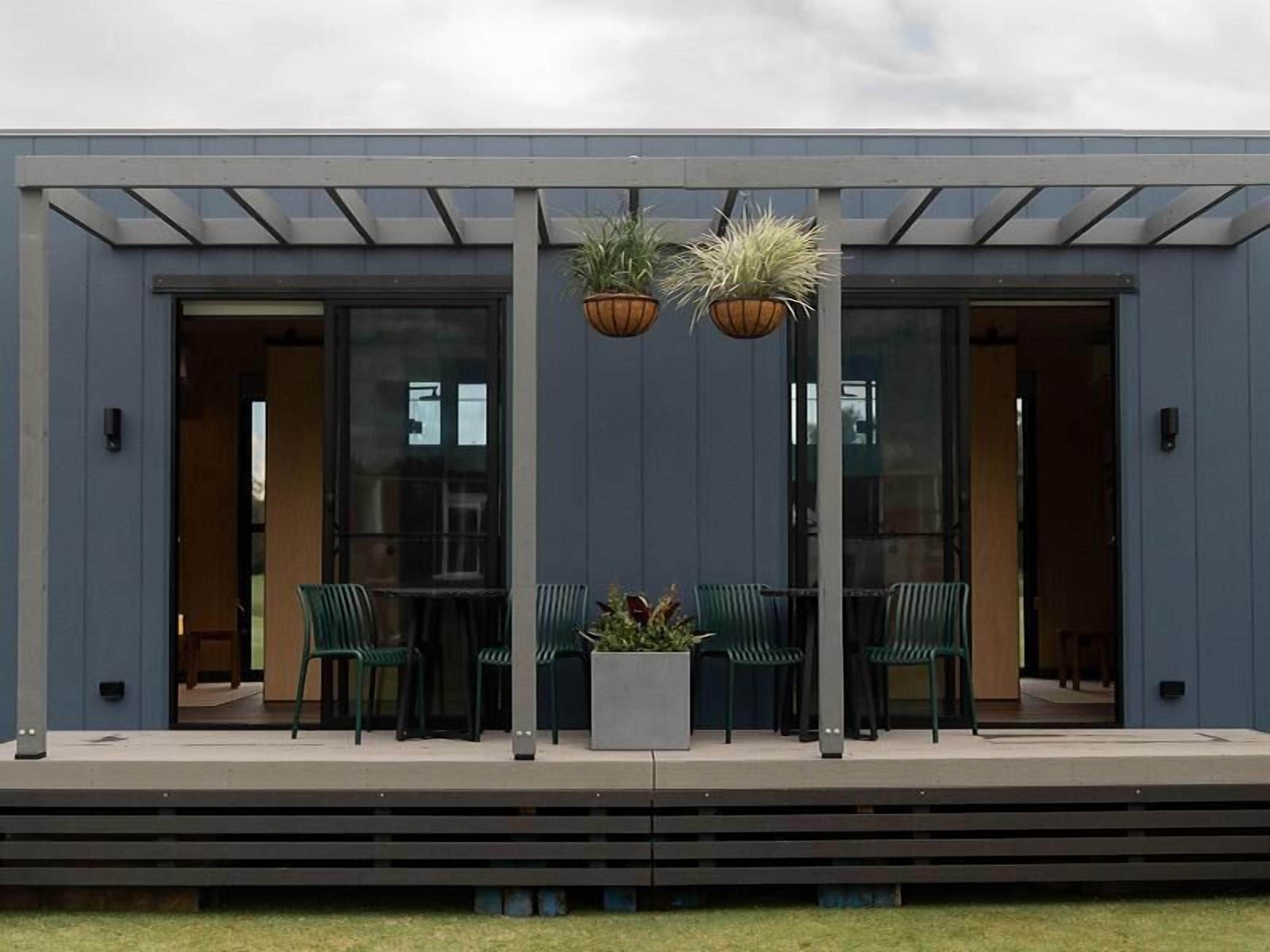 A modern building with a covered patio area featuring green chairs and potted plants.