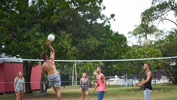 Un grupo de personas jugando voleibol en un campo cubierto de césped, con árboles al fondo.