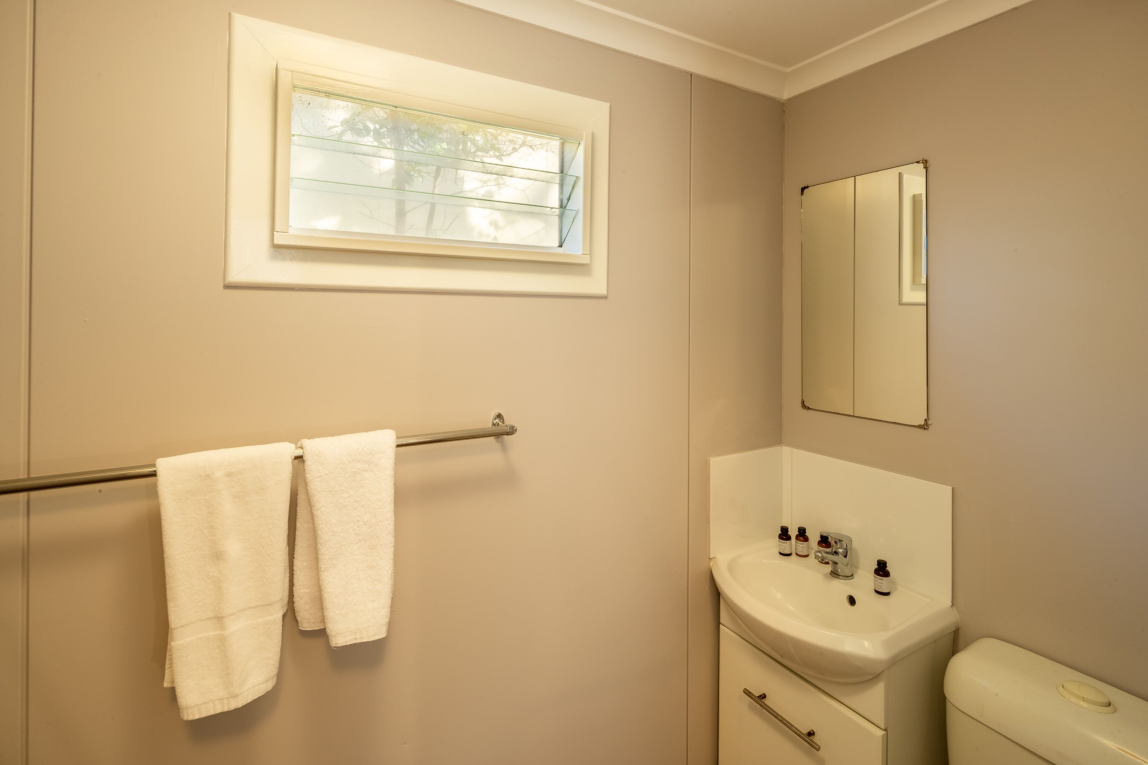 Une salle de bain avec une fenêtre, un porte-serviettes, un lavabo avec des articles de toilette et un miroir.
