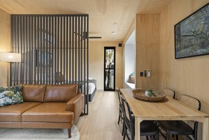 Una sala de estar moderna con un sofá de cuero marrón, una mesa de comedor de madera con sillas, una cesta decorativa y un cuadro abstracto grande en la pared.