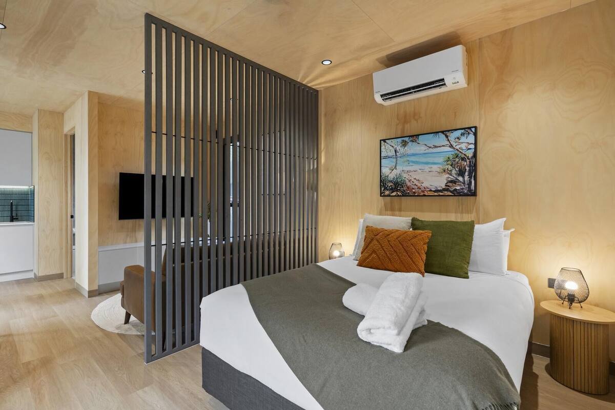 Ein modernes Hotelzimmer mit einem großen Bett, einem Fernseher, einer Klimaanlage und einem Bild mit einer Strandansicht.