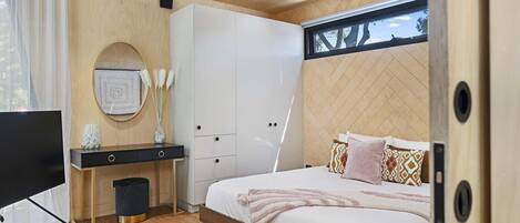 Een moderne slaapkamer met een houten plafond, een bed met gekleurde kussens, een nachtkastje met een vaas en een televisie.