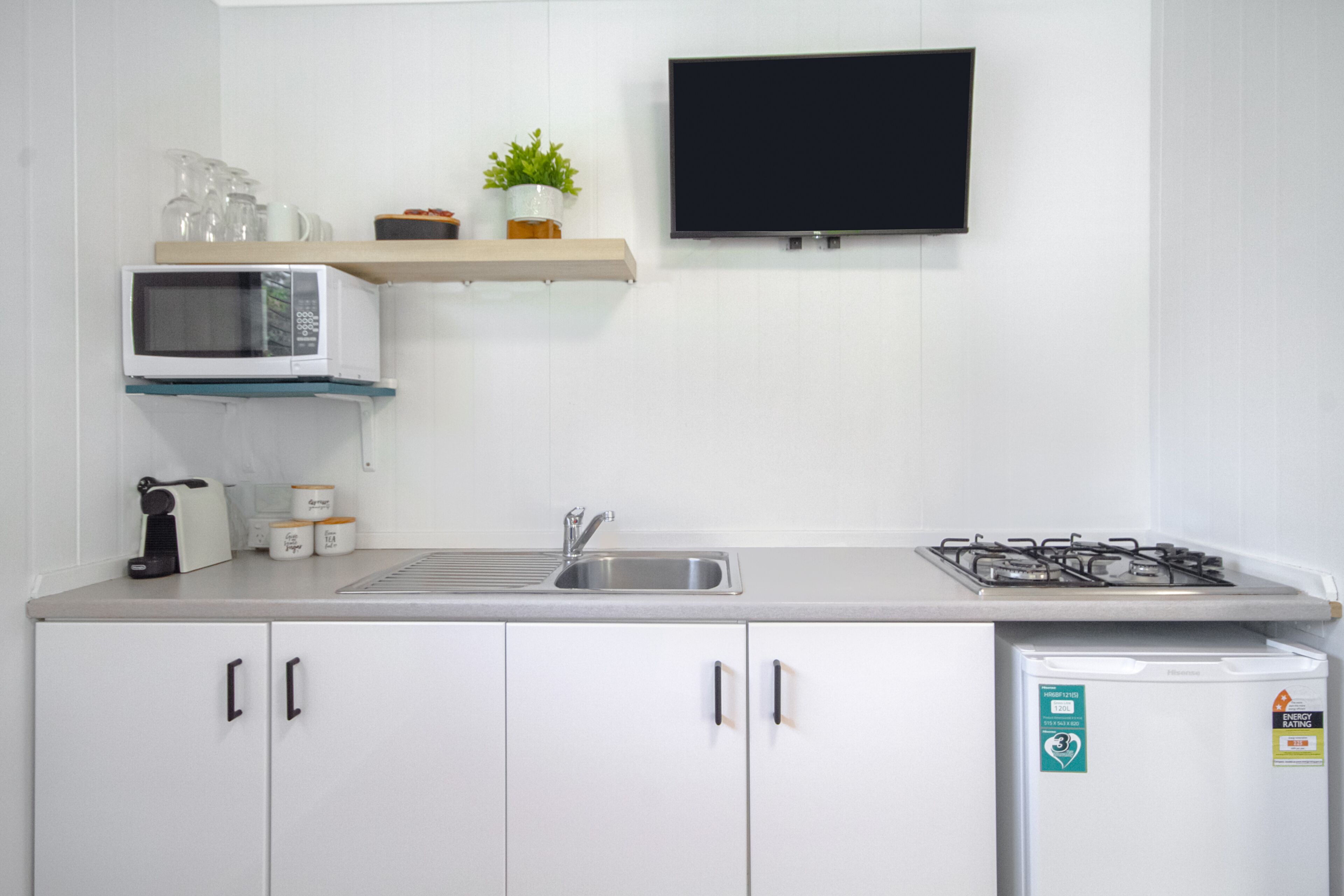 A modern kitchen with white cabinets, a microwave, a sink, a gas stove, and a small refrigerator.