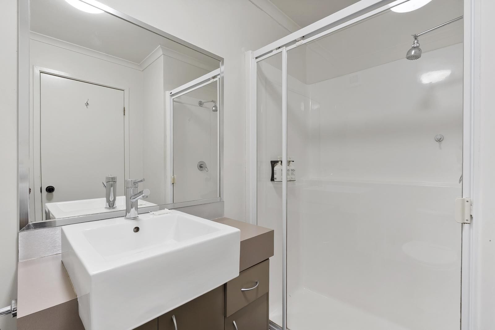 Un baño moderno con un lavamanos grande de color blanco, un espejo y una ducha con cerramiento de vidrio.