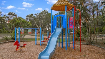 A playground with a slide, climbing structures, and a red horse-shaped swing set.