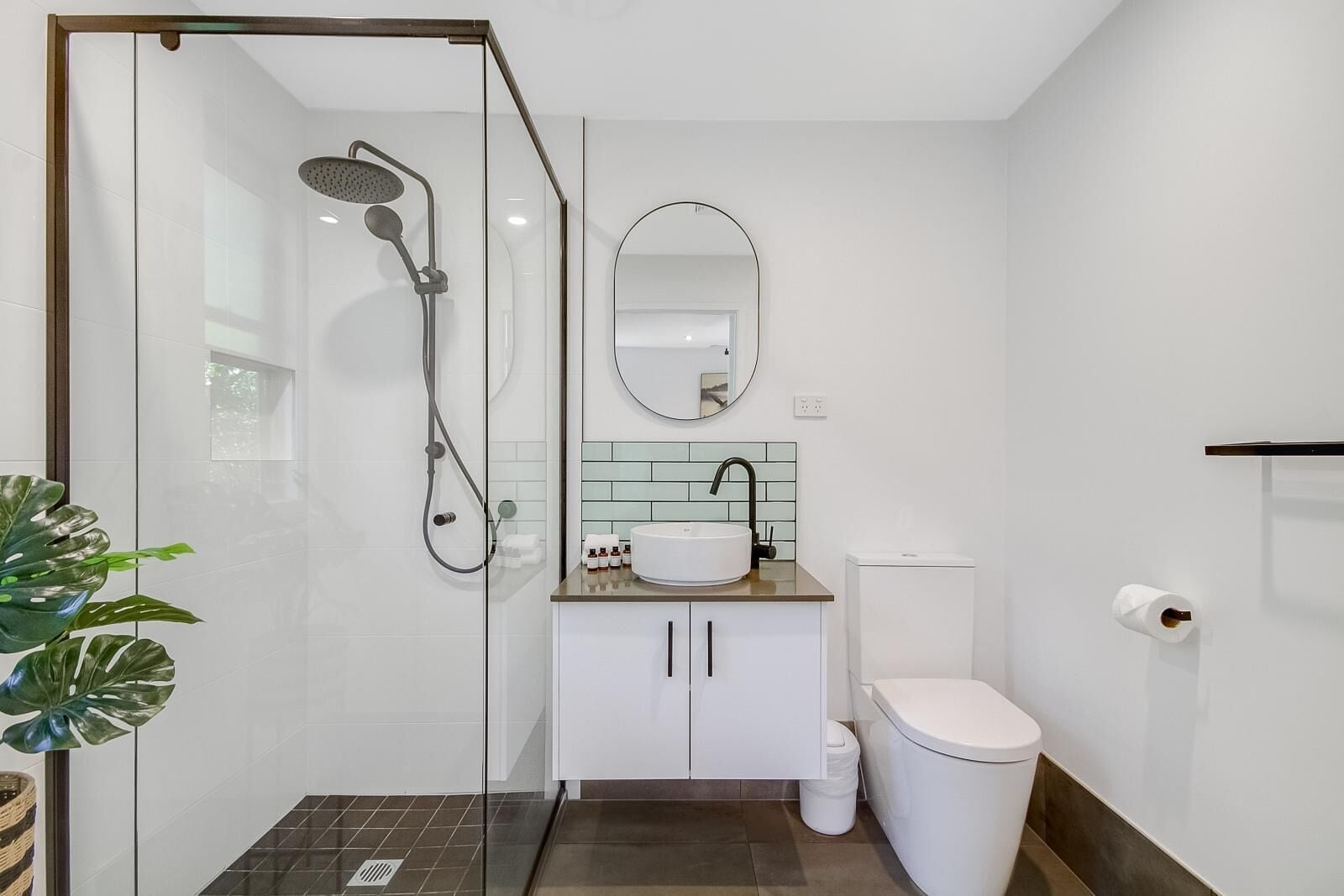 Un baño moderno con ducha de vidrio, lavamanos blanco con espejo arriba y retrete.