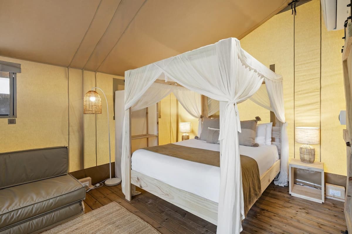 Ein Schlafzimmer mit einem Himmelbett, einer Couch, einem Nachttisch mit Lampe und einer Wandleuchte.