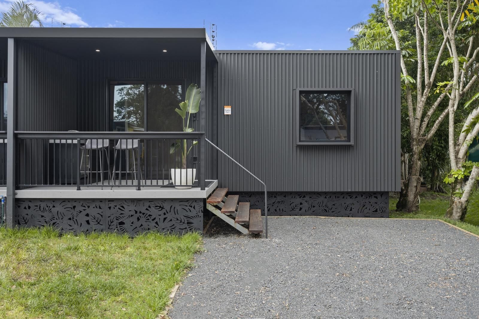 Un bâtiment moderne doté d’un espace extérieur couvert avec des sièges, d’un escalier menant à une terrasse et d’une petite fenêtre.