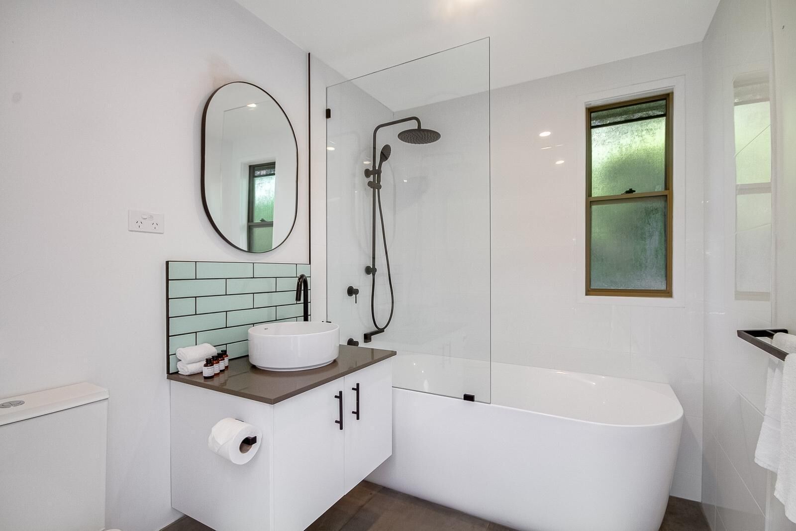 A modern bathroom with a freestanding bathtub, a round mirror, a white sink, and a glass-enclosed shower.