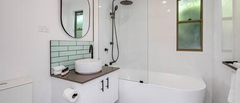 A modern bathroom with a freestanding bathtub, a round mirror, a white sink, and a glass-enclosed shower.