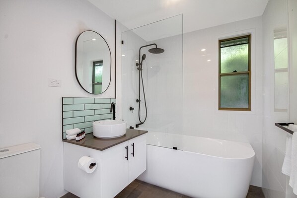 A modern bathroom with a freestanding bathtub, a round mirror, a white sink, and a glass-enclosed shower.